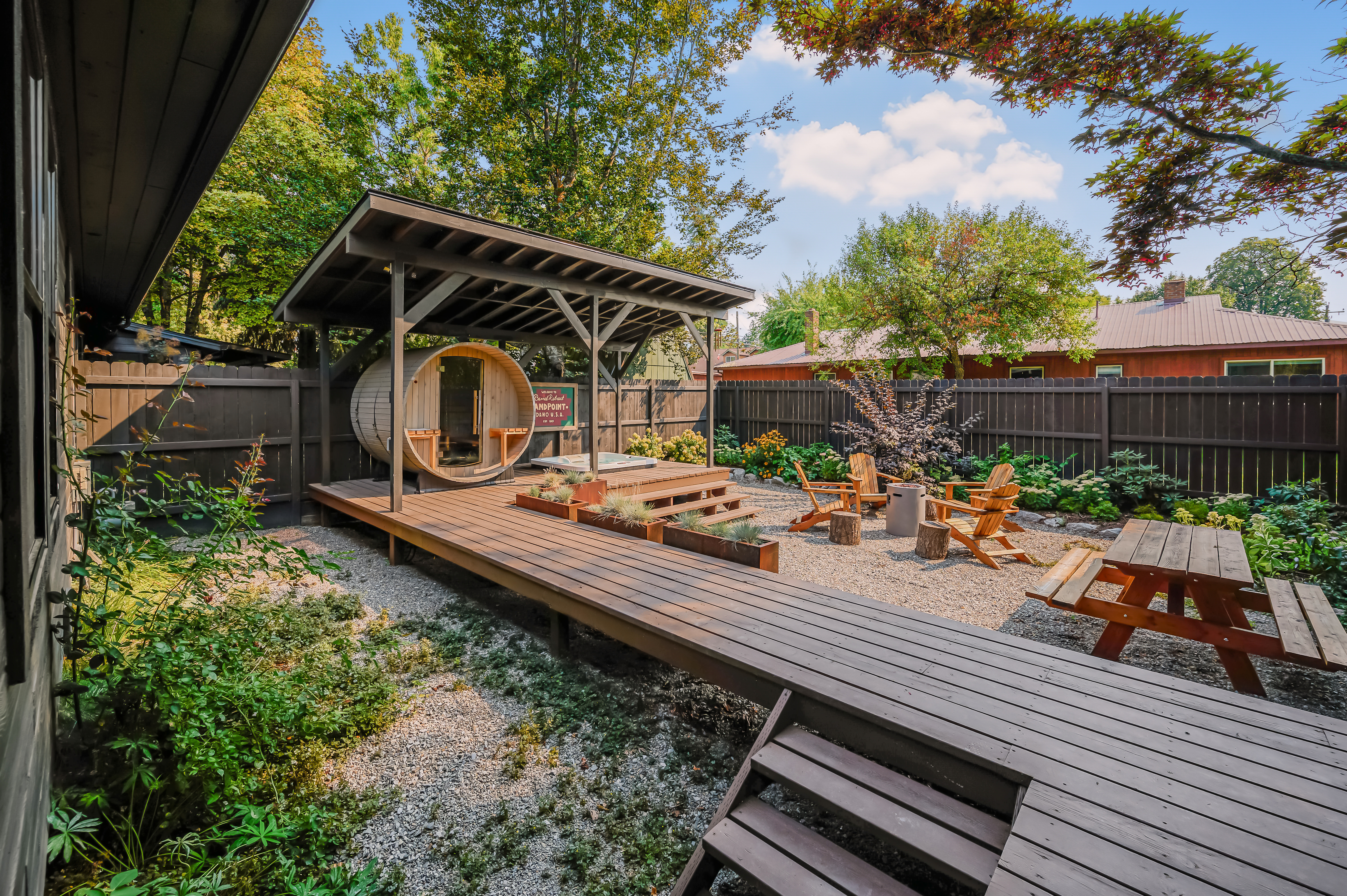 Daytime backyard with barrel sauna, fire pit, and deck